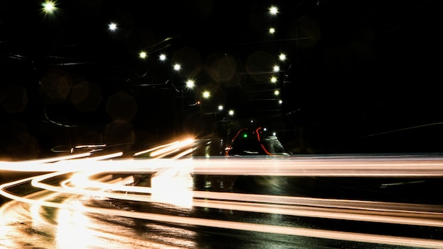 Feux de voitures la nuit. Lampadaires. Ville de nuit. Route de nuit de photographie à longue exposition. Bandes colorées de lumière sur la route. Route mouillée après la pluie.