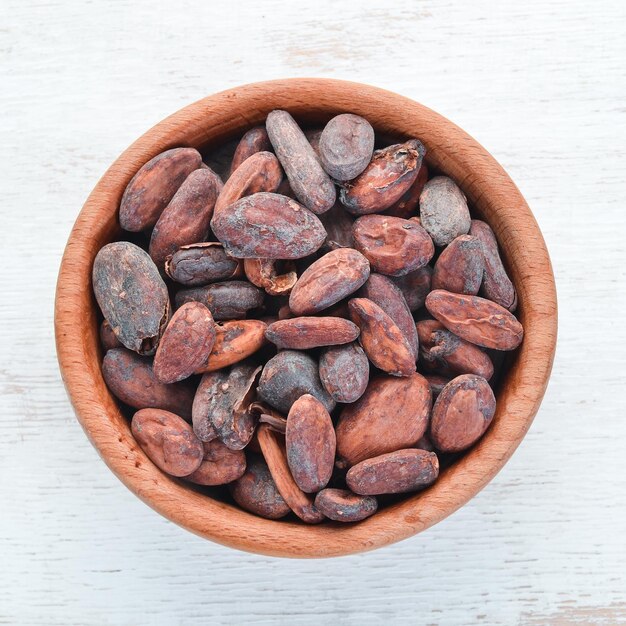 Fèves de cacao dans un bol sur un fond en bois blanc. Vue de dessus. Espace de copie gratuit.