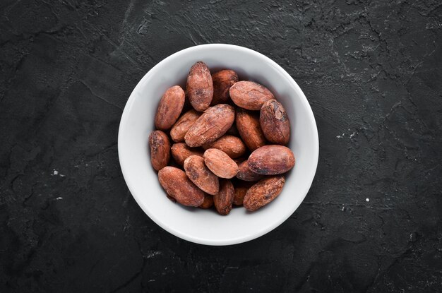 Fèves de cacao dans un bol sur fond noir Vue de dessus Espace de copie gratuit