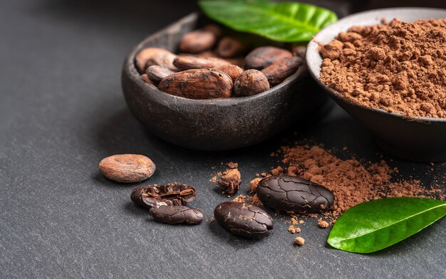 Fèves et poudre de cacao dans un vieux bol en bois avec des feuilles