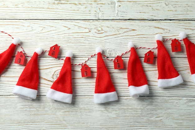 Ficelle avec des maisons rouges et des chapeaux de Père Noël sur fond de bois blanc.