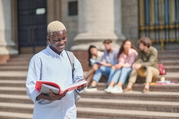 Fier étudiant avec un manuel debout devant l'université