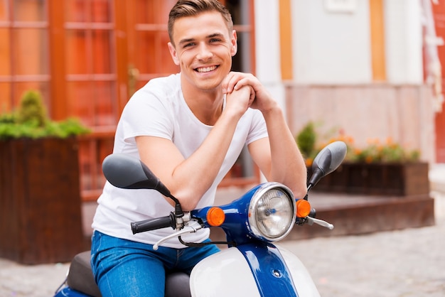 Fier de son nouveau scooter. Beau jeune homme assis sur un scooter et souriant