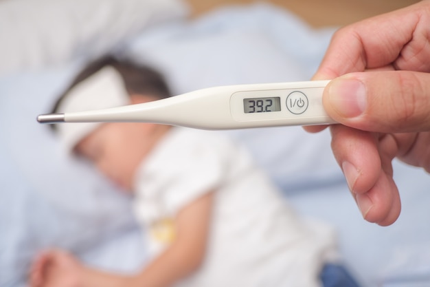 Fièvre, thermomètre médical en gros plan, parent / père mesurant la température de son enfant malade, garçon asiatique de 3 à 4 ans, fièvre élevée