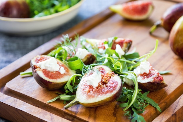 Figue avec fromage de chèvre et salade de roquette sur planche à découper en bois