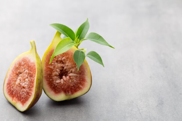 Figues entières et une figue coupée en deux sur une table grise.