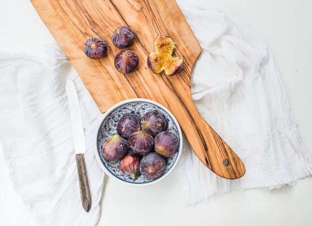 Figues fraîches dans un bol en céramique à motifs bleu et sur une planche en bois d'olivier sur un tissu blanc