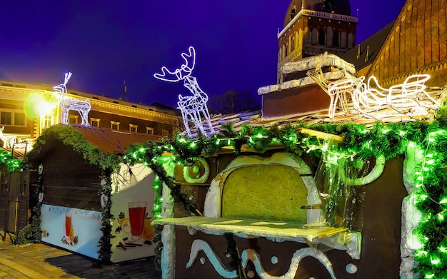 Figure de cerf lumineuse sur le dessus du décrochage pendant le marché de Noël dans le vieux Riga, Lettonie. Hiver. Tard le soir. Foire de rue et de vacances dans la ville européenne Décoration de l'Avent avec des objets d'artisanat sur le bazar