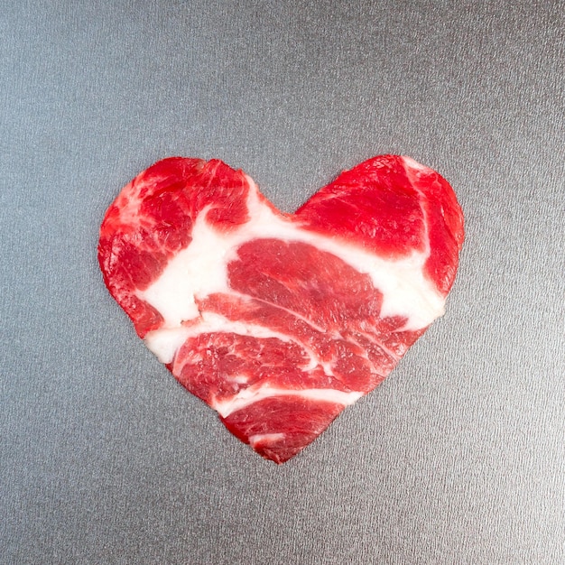 Figure coeur sur une poêle en téflon tapissée de morceaux de viande crue