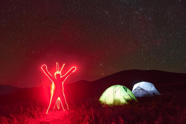 Figure de l'homme par l'éclairage au néon Deux tentes éclairées sous les étoiles à la montagne la nuit