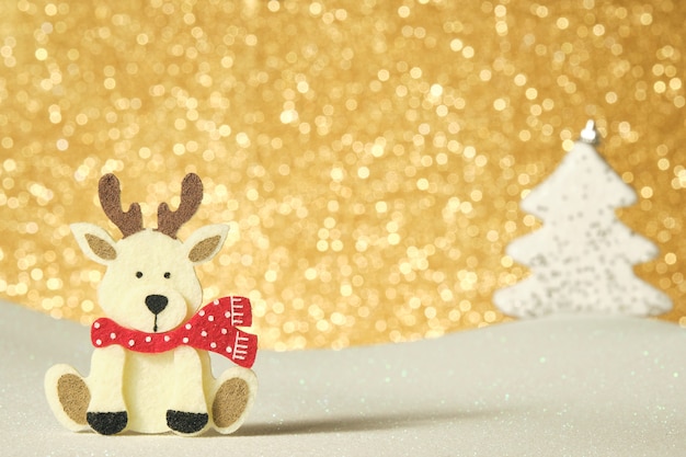 Figure de renne en feutre sur fond d'or brillant sur une surface blanche brillante avec un arbre de Noël à fond blanc