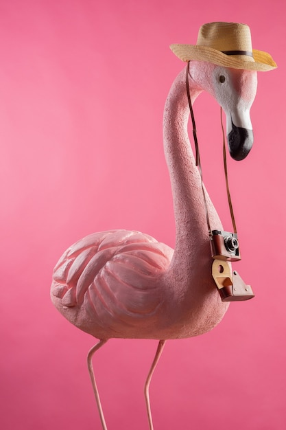 Figure d'un touriste flamant rose dans un chapeau de paille tenant un appareil photo