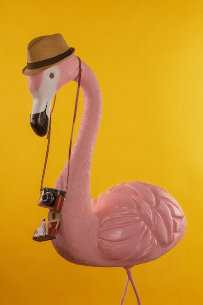 Figure d'un touriste flamant rose dans un chapeau de paille tenant un appareil photo