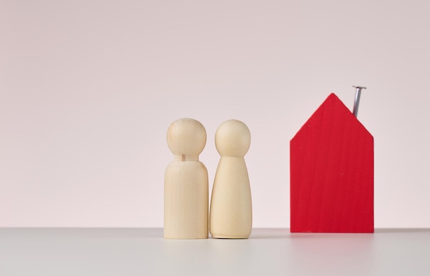 Figures en bois d'hommes et d'une maison miniature sur fond beige Le concept d'achat ou de vente d'hypothèque immobilière et d'assurance immobilière