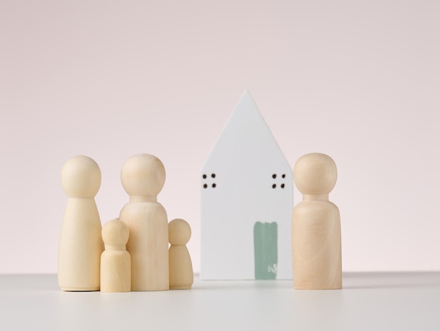 Figures en bois d'hommes et d'une maison miniature sur fond beige Le concept d'achat ou de vente d'hypothèque immobilière et d'assurance immobilière