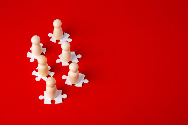 Figures en bois sur des puzzles sur fond rouge comme symbole de l'esprit d'équipe Groupe d'organisation de personnes en affaires