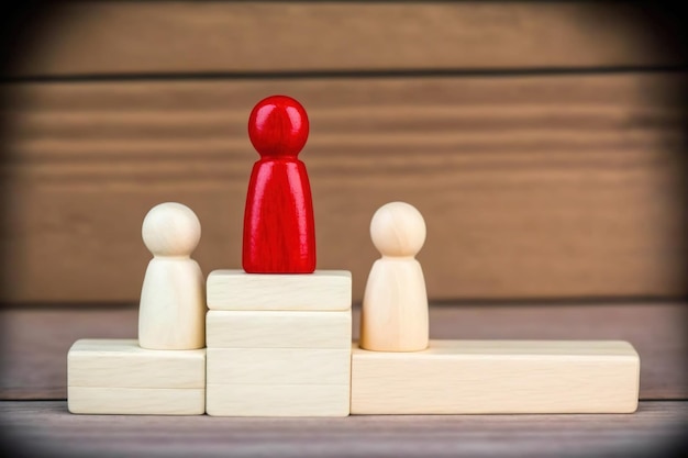 Figures en bois sur une table, une figure rouge se dresse sur un podium.