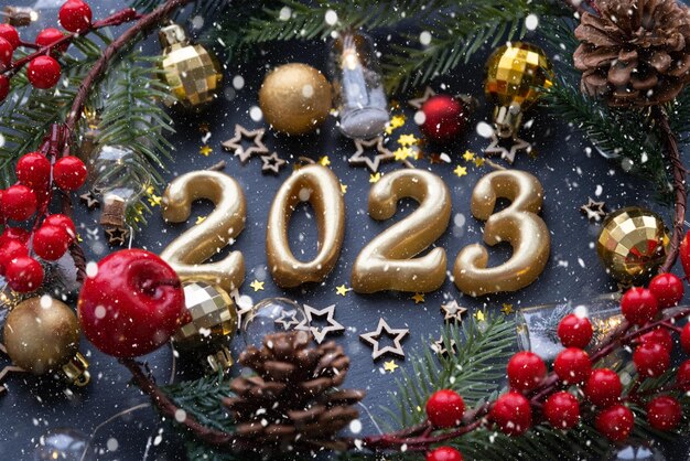 Les figures dorées 2023 faites de bougies sur fond d'ardoise en pierre noire sont ornées d'un décor festif d'étoiles paillettes branches de sapin boules et guirlandes Carte de voeux bonne année