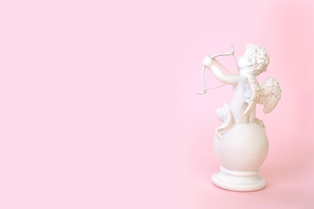 Figurine d'un ange Cupidon avec un arc sur un mur rose. La Saint-Valentin.