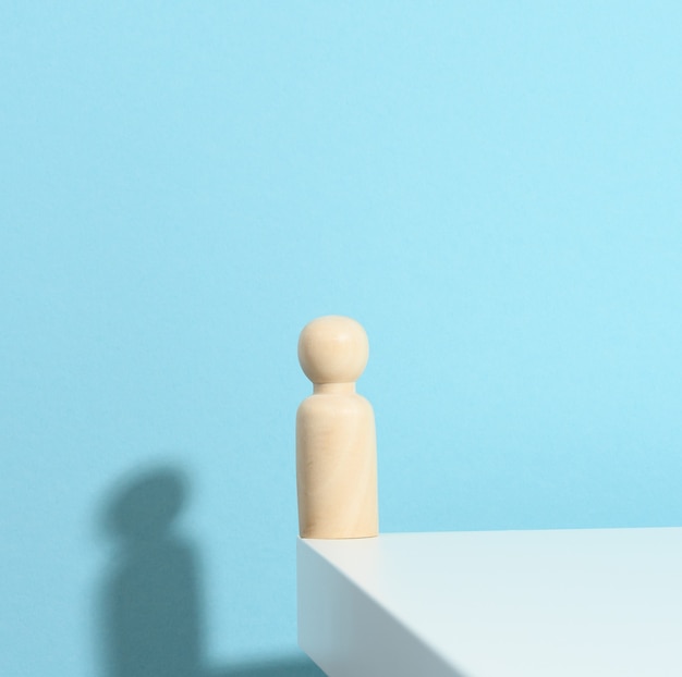 Figurine en bois d'un homme sur fond bleu avec une ombre. Le concept de solitude, de tristesse et de nostalgie