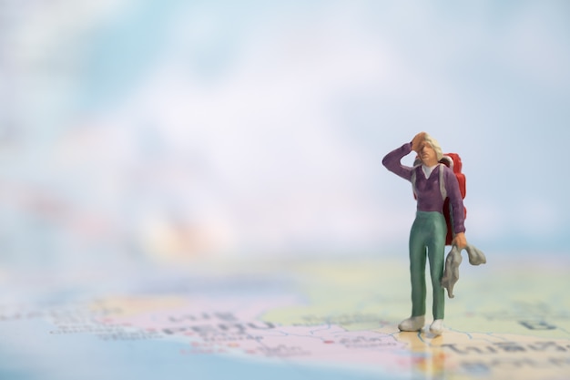 Figurine miniature voyageur avec sac à dos debout et reste sur la carte du monde.