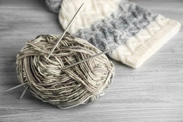 Fil et aiguilles tricotés de chapeau sur le fond en bois gris