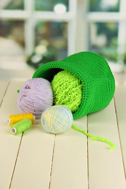 Fil coloré pour tricoter dans un panier vert sur une table en bois sur fond de fenêtre