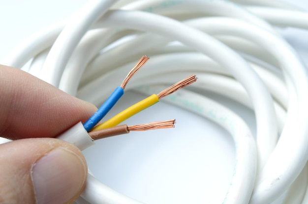 Un fil électrique à trois fils dénudé dans une main sur le fond d'un fil torsadé dans une bobine.