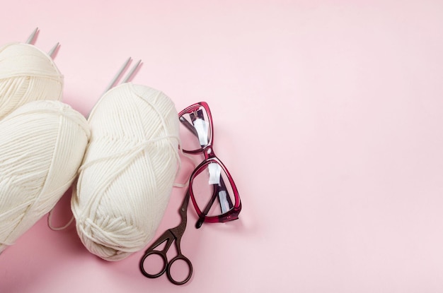 Fil de laine beige avec des aiguilles à tricoter sur fond rose pour le tricot