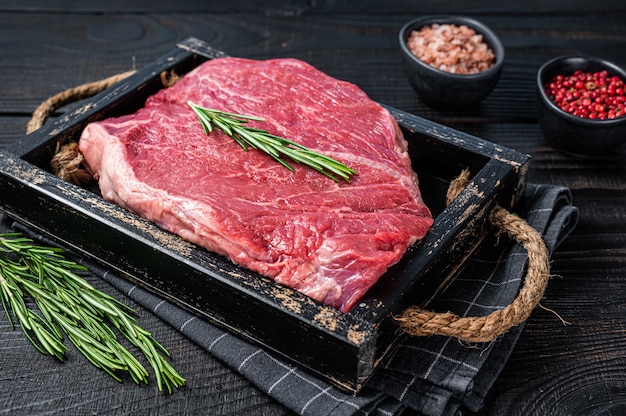 Filet de boeuf cru pour steaks dans un plateau en bois aux herbes. Fond en bois noir. Vue de dessus.