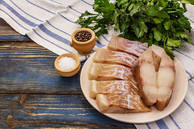 Filet cru de lieu noir. Tranches fraîches sur une assiette, épices, persil. Un tas de verts, serviette vintage