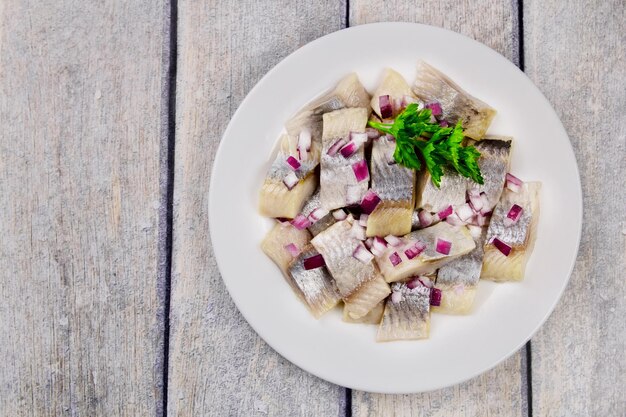 Filet de hareng méditerranéen servi sur une assiette avec de l'oignon haché et du persil sur la table