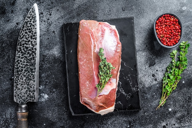 Filet de magret de canard cru sur une planche de marbre. Fond noir. Vue de dessus.