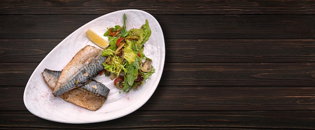 Filet de maquereau au four avec salade et champignons sur une assiette sur un fond en bois