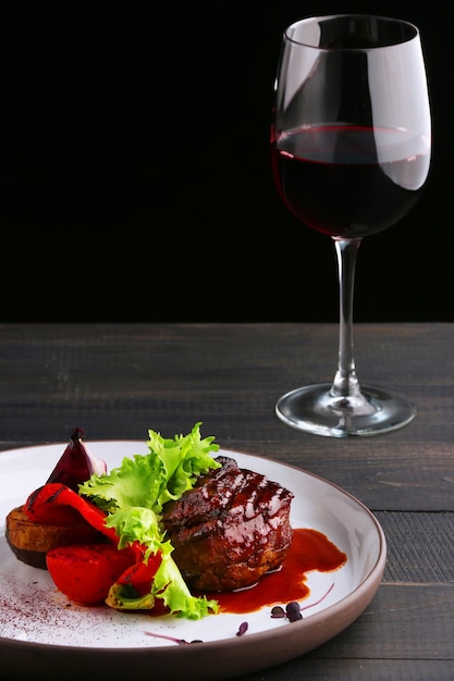 Filet Mignon Avec Salade De Légumes Et Verre De Vin Rouge. Assiette Avec Filet Mignon Sur Table En Bois Et Fond Noir.