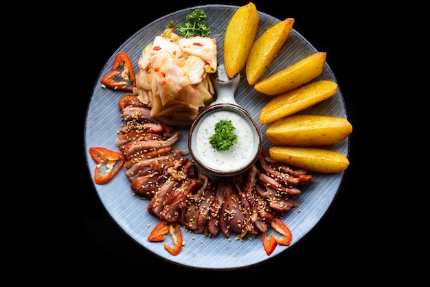 Filet d'oie frit à l'ail servi avec des quartiers de pommes de terre et du kim chi sur fond noir vue de dessus