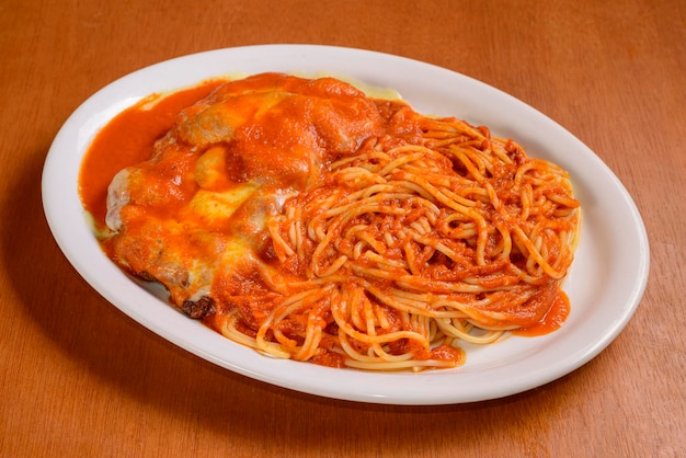 Filet Parmigiana avec sauce tomate et pâtes dans un bol blanc sur une table en bois Plat populaire au Brésil