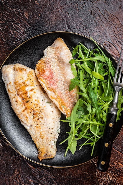 Photo filet de perche rouge de mer roasted snapper sur une assiette avec salade fond sombre vue de dessus