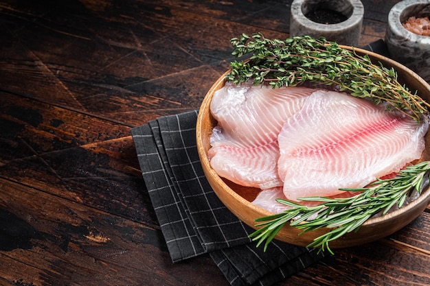 Filet de poisson blanc tilapia cru dans une assiette en bois avec du romarin et du thym Fond en bois Vue de dessus Espace de copie