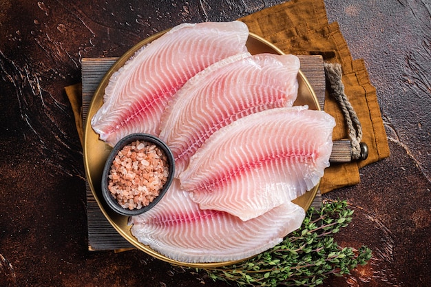 Filet de poisson cru de tilapia dans une assiette aux épices Fond sombre Vue de dessus