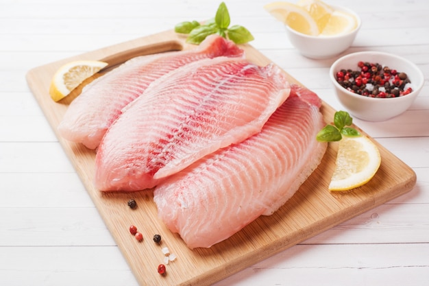 Filet de poisson cru de tilapia sur une planche à découper au citron et épices