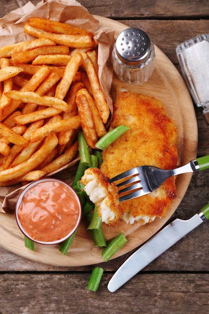 Filet de poisson frit pané et pommes de terre aux asperges et sauce sur une planche à découper et en bois rustique