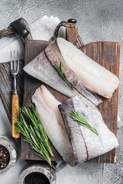 Filet de poisson Haddock, viande de fruits de mer crue sur planche de bois aux herbes. Fond blanc. Vue de dessus.