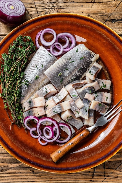 Filet de poisson hareng mariné mariné sur une assiette avec du thym et l'oignon sur une table en bois. Vue de dessus.