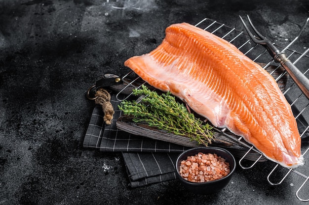 Filet de poisson saumon cru cuisson des steaks sur le gril avec des herbes Fond noir Vue de dessus Espace de copie