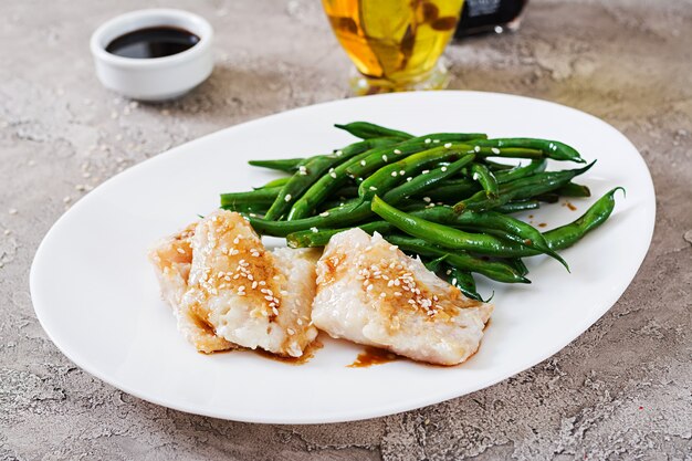 Filet de poisson servi avec sauce soja et haricots verts dans une assiette blanche. Nourriture asiatique.