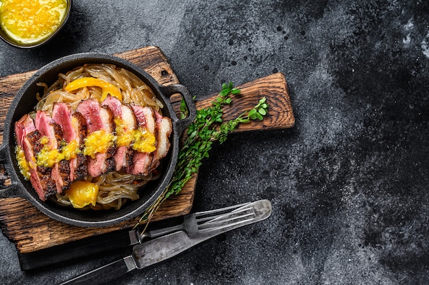 Filet de poitrine de canard grillé avec sauce aux nouilles et mandarines. Fond noir. Vue de dessus. Copiez l'espace.