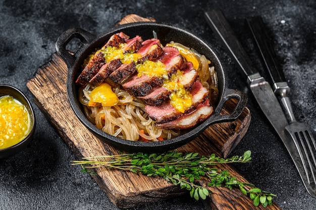 Photo filet de poitrine de canard grillé, sauce nouilles et mandarines. table noire. vue de dessus.