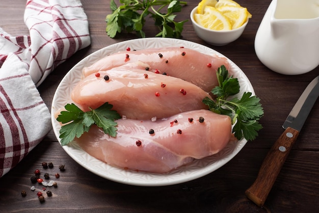 Filet de poitrine de poulet cru sur une assiette, fond en bois foncé.