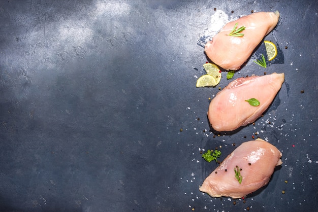 Filet de poitrine de poulet cru sur fond de béton foncé avec des épices et des herbes pour la cuisson, espace de copie vue de dessus